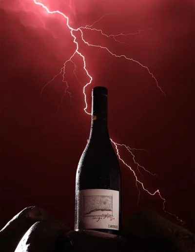 Mise en scène d'une bouteille de vin sur des rochers avec un ciel rouge et un éclair derrière, réalisée par un photographe à Annecy