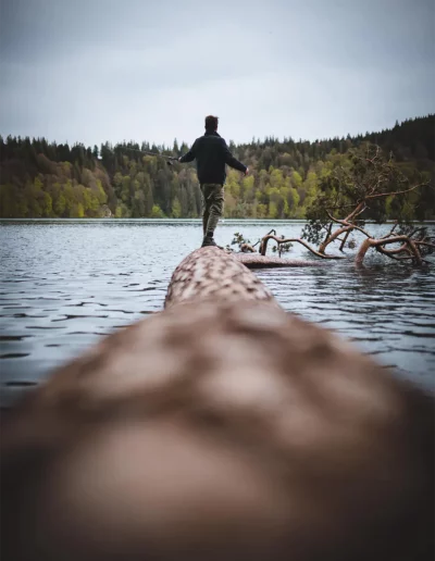 un homme pêche en équilibre sur un tronc d'arbre sur un lac